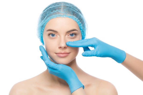 Young woman ready for rhinoplasty, doctor in blue gloves touching her nose, isolated on white background Young woman ready for rhinoplasty, doctor in blue gloves touching her nose, isolated on white background plastic surgery photos stock pictures, royalty-free photos & images