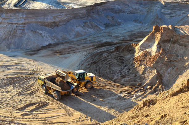 radlader entlädt sand in bergbau-lkw am tagebau - front end loader construction vehicle metal industry mining stock-fotos und bilder