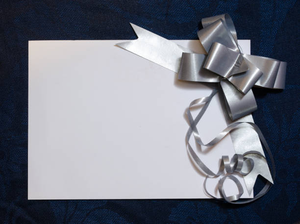 istock White card close up with silver or gray gift bow on blue cloth background. Celebration, Christmas, Mother's day, Father's day or invitation concept. 1280644842