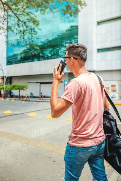 istock A handsome young man walking, going to work, using his mobile phone, selfie, wearing a protective mask over his face 1280655996
