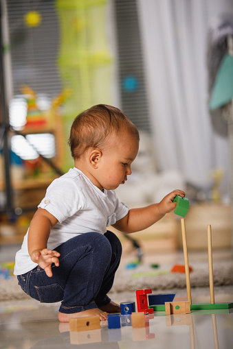Side view of little boy developing his motor sensory skills while playing with colorful wooden toys on the floor.