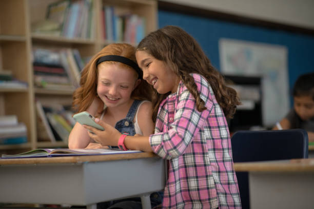 istock Elementary girls playing on a phone together during class 1280660064