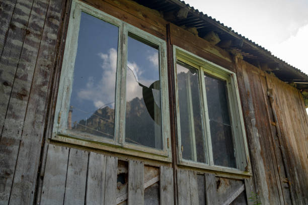 istock Window with broken glass in old building. Wooden window frame with partially broken glass in old abandoned wooden building 1280662679