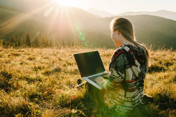 Hipster woman working with laptop sitting in mountains. Hiker tourist enjoying valley view sunset. Vacation holidays in autumn day. Distant remote work and travel, freelance as lifestyle concept. mujer hipster trabajando con portátil sentado en las montañas. turista excursionista disfrutando de la puesta de sol vista del valle. vacaciones en el día de otoño. trabajo y viajes remotos distantes, freelance como concepto de estilo de vida.