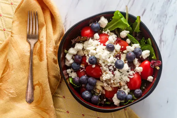 Bowl of blueberry fruit salad with crumbled goat cheese and almonds
