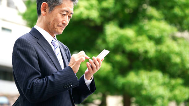 中年のアジアのビジネスマンは、スマートフォンを使用しています。 - スマホ 日本人 ストックフォトと画像