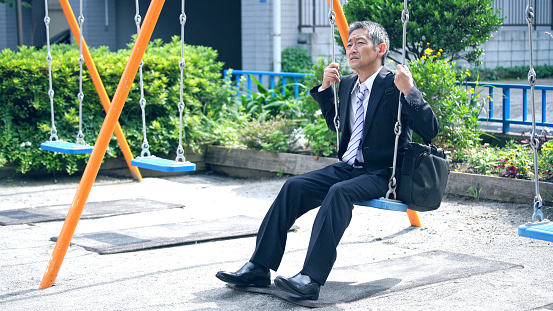 Middle aged asian businessman riding on swing.