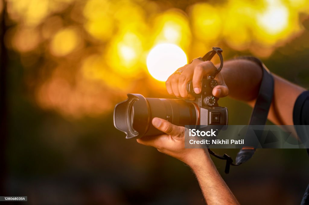 Jalgaon, Maharashtra / India - May 4, 2020 : Closeup of a black camera holding by Photographer's hand with sunset background Digital Single-Lens Reflex Camera Stock Photo