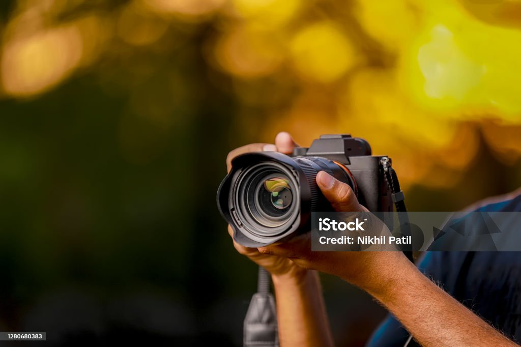 Jalgaon, Maharashtra / India - May 4, 2020 : Closeup of a black camera holding by Photographer's hand with sunset background Camera - Photographic Equipment Stock Photo
