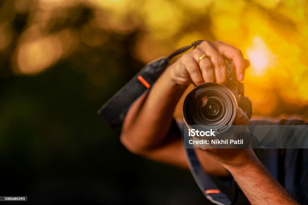 Jalgaon, Maharashtra / India - May 4, 2020 : Closeup of a black camera holding by Photographer's hand with sunset background Camera - Photographic Equipment Stock Photo
