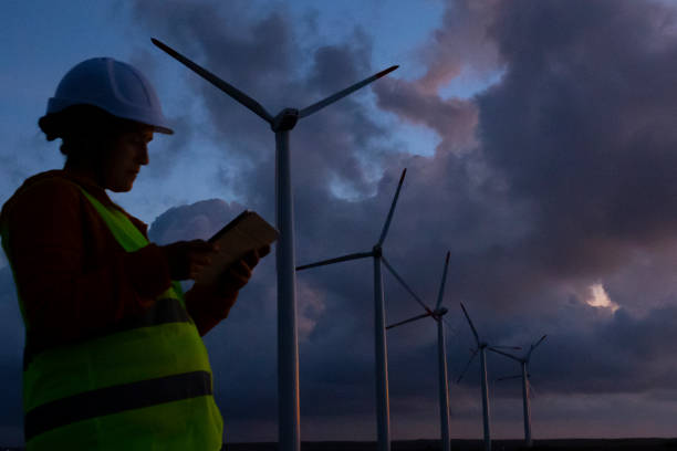 istock Renewable Energy Systems. Electricity Maintenance Engineer working on the field at a Wind Turbine Power station at dusk. 1280694959