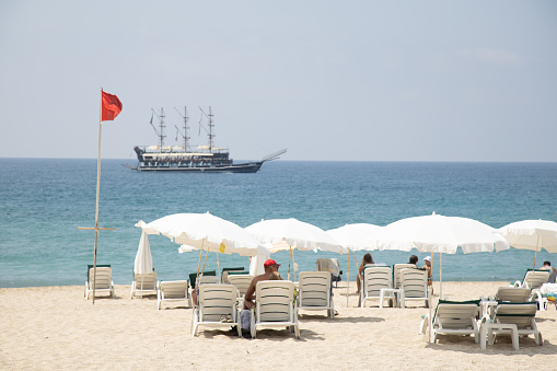 Alanya, Turkey - 28 Aug, 2020: Shore line with tourist recreational ships parked on it with mountains covered in clouds. Red flag indicates no lifeguard service due to stormy conditions. Antalya recreational season this year