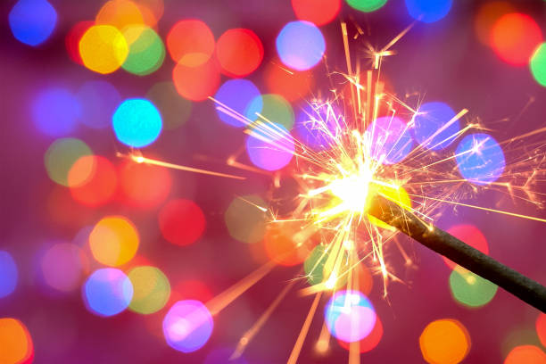 istock Bright burning sparkler against the backdrop of defocused multicolored garland. Blurred backdrop. Merry Christmas or birthday holiday concept. 1280700633