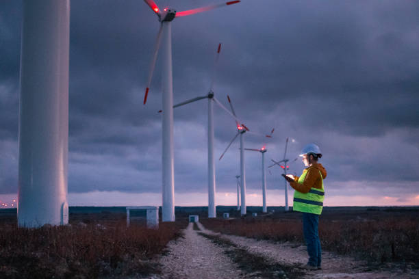 istock Renewable Energy Systems. Electricity Maintenance Engineer working on the field at a Wind Turbine Power station at dusk with a moody sky behind. Blurred motion. 1280703365