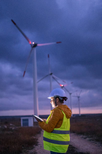 erneuerbare energiesysteme. strom-wartungsingenieur arbeitet auf dem feld in einem windturbinenkraftwerk in der dämmerung mit einem launischen himmel dahinter. verschwommene bewegung. - industry dusk night sustainable resources stock-fotos und bilder