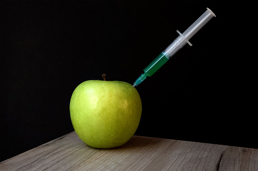Green apple on a wooden board and syringe inside it extracting green liquid