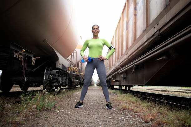 portrait of sexy sportswoman proudly standing between trains and smiling to the camera. fitness and sport. - railing beautiful human leg people imagens e fotografias de stock