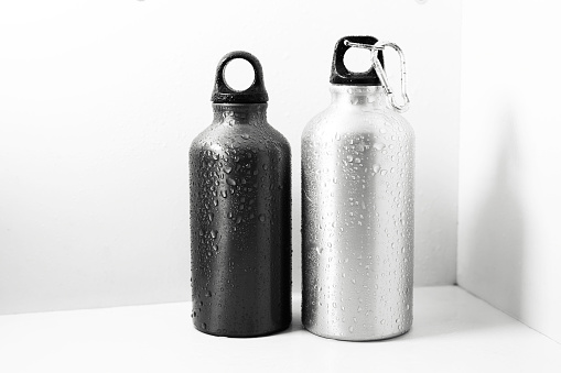Close-up of black and silver, reusable aluminum thermo bottle sprayed with water, isolated on white background.