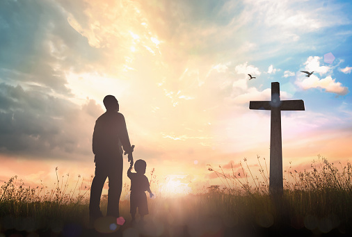 Silhouette father and son looking for the cross on meadow autumn sunrise background