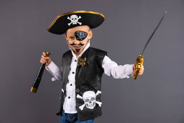 A pirat captain with a painted seriously face with a sword and a telescope in his hands. Isolated on gray background. Happy Halloween