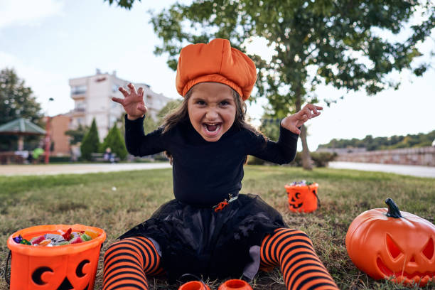istock Spooky girl in a witch costume making scary face while sitting on the grass after she finished with trick or treat 1280713092