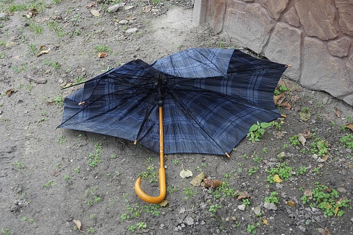 one blue broken umbrella with brown wooden handle lies on gray ground outside