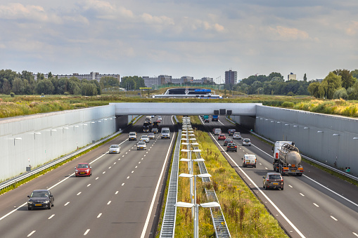 Afternoon traffic on a4 motorway near The Hague Randstad area. Highway crossing aquaduct tunnel with urban area of Rotterdam in backdrop, Netherlands.