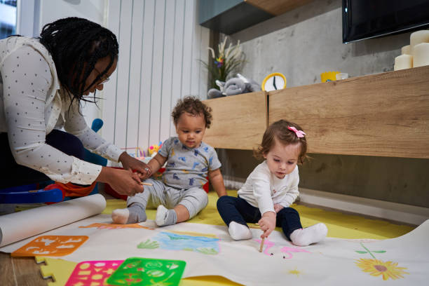 Caring nanny Black ethnicity taking care of babies while they using their creativity to draw on a paper