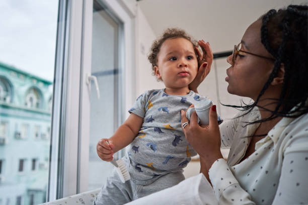 istock Calm baby boy sitting on a change bed while his mother applying a lotion on his face 1280721012