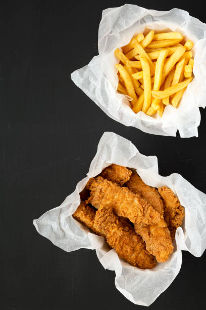 istock French Fries and Fried Chicken Strips on a black surface, view from above. Overhead, flat lay, top view. Copy space. 1280731476