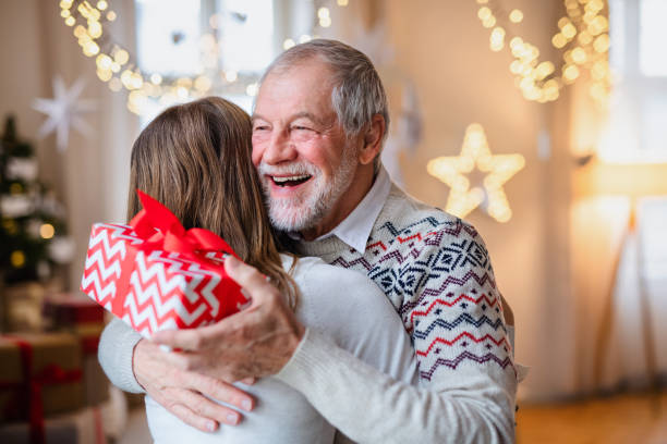 młoda kobieta dająca prezent szczęśliwemu dziadkowi w domu na boże narodzenie. - giving christmas lifestyles holiday zdjęcia i obrazy z banku zdjęć