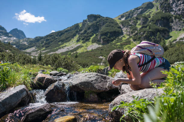 Girl hiker refreshing her face at the mountain stream