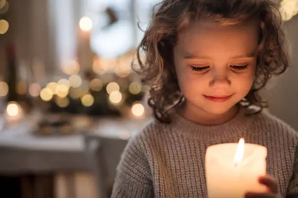 Photo of Cheerful small girl indoors at home at Christmas, holding candle.
