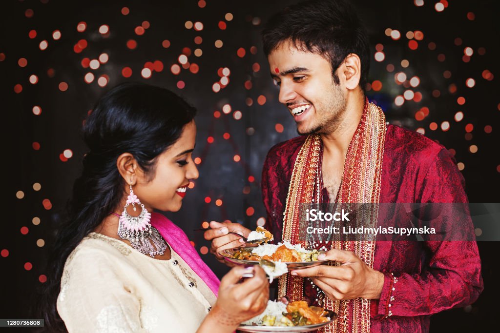 Couple eating during Indian festival Beautiful Indian couple eating food over festive bokeh background Culture of India Stock Photo