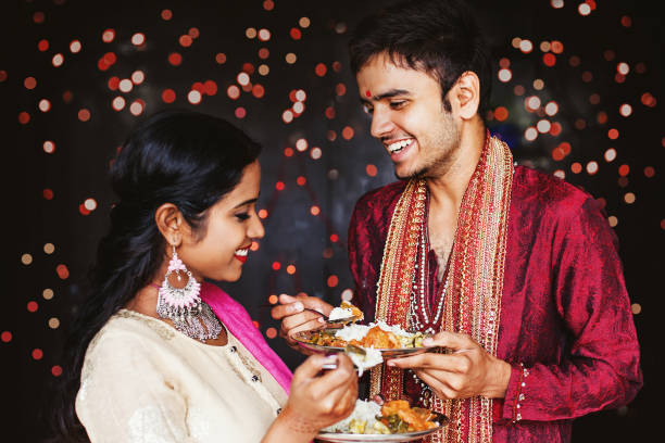 Couple eating during Indian festival Beautiful Indian couple eating food over festive bokeh background indian dinner stock pictures, royalty-free photos & images