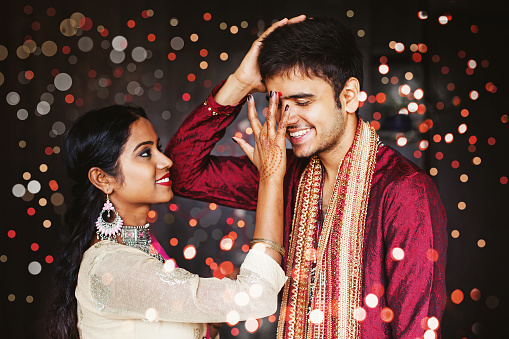Indian woman is giving blessings to the brother by putting tika on his forehead. Both wearing traditional ethnic clothes. Bokeh on a background
