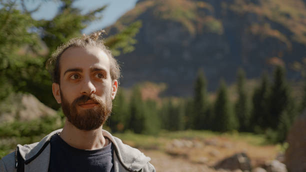istock Hipster man with long beard with backpack behind him is looking towards the camera with a confused facial expression and thinks, lifestyle and nature concept 1280738211