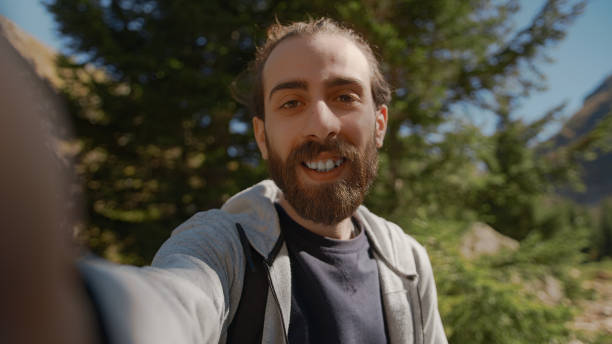 istock Hippie climber with his backpack behind him, with his handheld camera or phone, salutes the audience or the person he is talking, vlogger or video chat in nature concept 1280738576