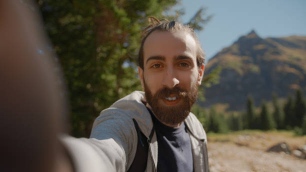 istock Hippie climber with his backpack behind him, with his handheld camera or phone, salutes the audience or the person he is talking, vlogger or video chat in nature concept 1280738613