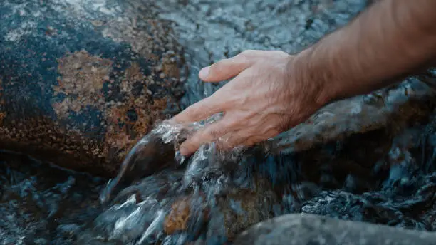 Photo of Person hand put in the flowing river or stream and is captivated by the water, close-up slow motion lifestyle nature concept