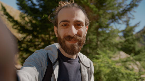 istock Hippie climber with his backpack behind him, with his handheld camera or phone, salutes the audience or the person he is talking, vlogger or video chat in nature concept 1280740246