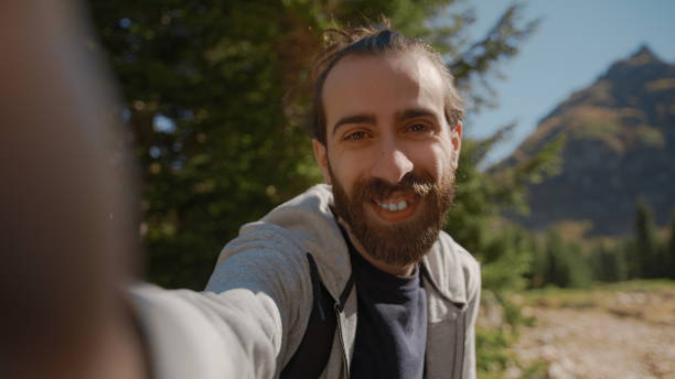 istock Hippie climber with his backpack behind him, with his handheld camera or phone, salutes the audience or the person he is talking, vlogger or video chat in nature concept 1280740728