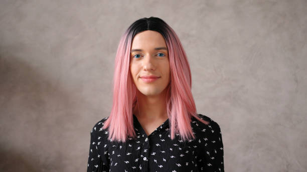 Transwoman in black dot dress with pink wig poses on beige Attractive young transwoman in stylish black dot clothes with bright pink wig poses for camera on beige color background closeup transgender person photos stock pictures, royalty-free photos & images