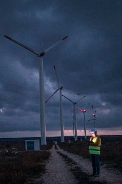 istock Renewable Energy Systems. Electricity Maintenance Engineer working on the field at a Wind Turbine Power station at dusk with a moody sky behind. Blurred motion. 1280744231