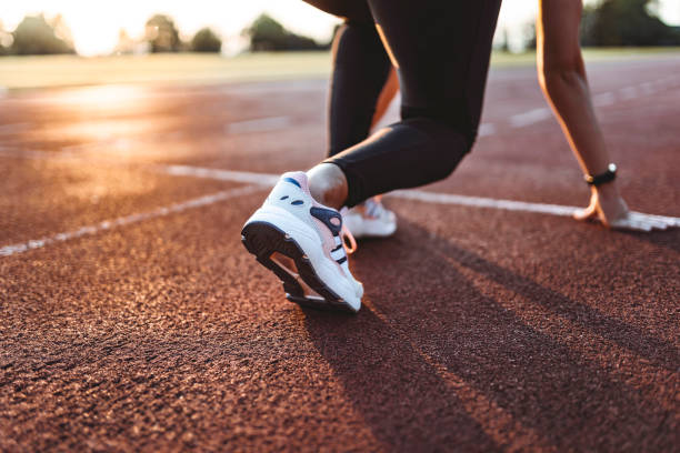 Close up of female athlete getting ready to start running on track . Focus on sneakers Ready to go! Close up cropped low angle photo of shoe of female athlete on the starting line of a stadium track, preparing for a run. Sunny spring day starting line stock pictures, royalty-free photos & images