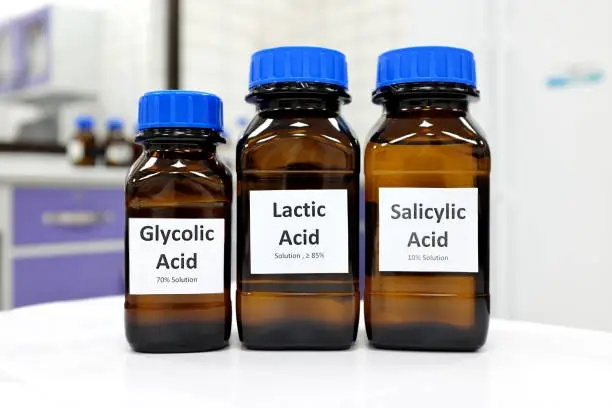 Photo of Selective focus of salicylic, lactic and glycolic acid liquid solution in dark brown glass bottle in a white chemistry laboratory background. Chemical peel for skin care research cosmetics industry.