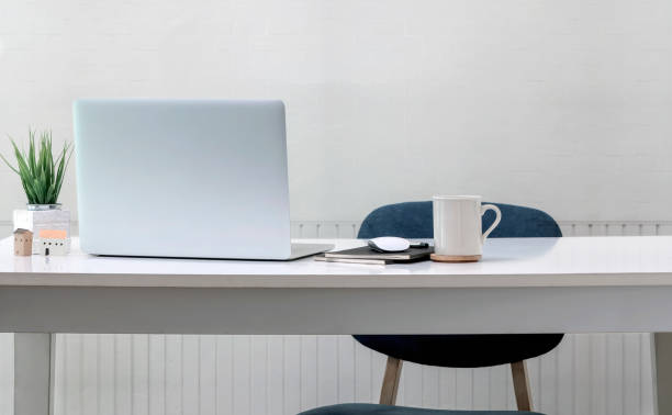 Home office concept. Mockup laptop computer with supplies on white top table in white room.