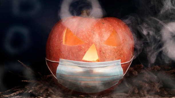 istock Halloween carved pumpkin glowing with protective medical face mask, coronavirus and quarantine concept, covid-19 halloween costume. eyes change brightness. White smoke. 1280761514