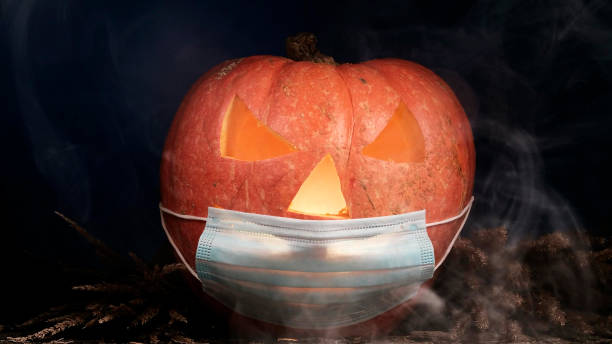 istock Halloween carved pumpkin glowing with protective medical face mask, coronavirus and quarantine concept, covid-19 halloween costume. eyes change brightness. White smoke. head turns clockwise 1280761919