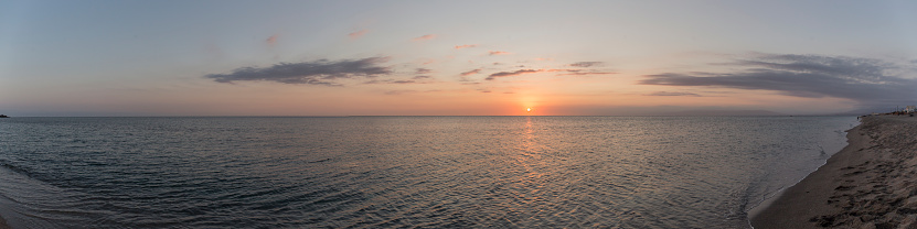 Panoramic of a beautiful sunset in the sea, the water is calm and the sky has orange colors, the clouds are dyed with color and the birds fly in the sky